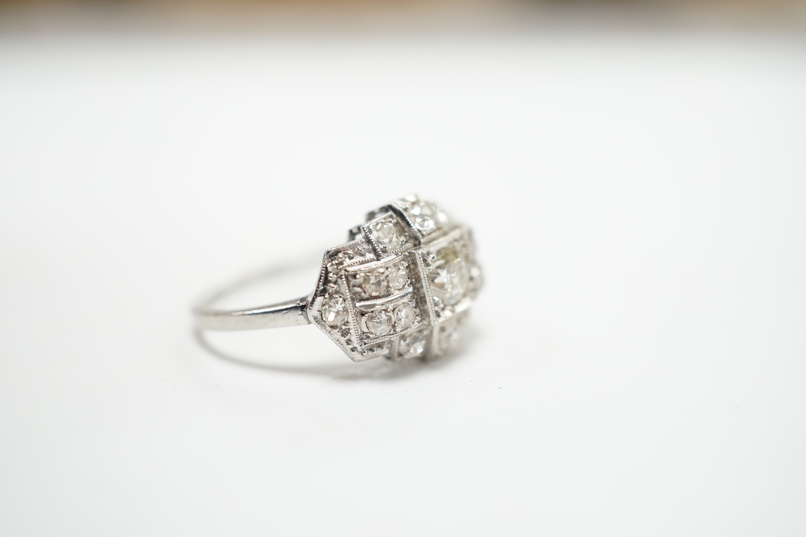 An Art Deco style white metal and millegrain set diamond cluster ring, size N/O, gross weight 4.1 grams, the central stone with a diameter of approximately 4.5mm.